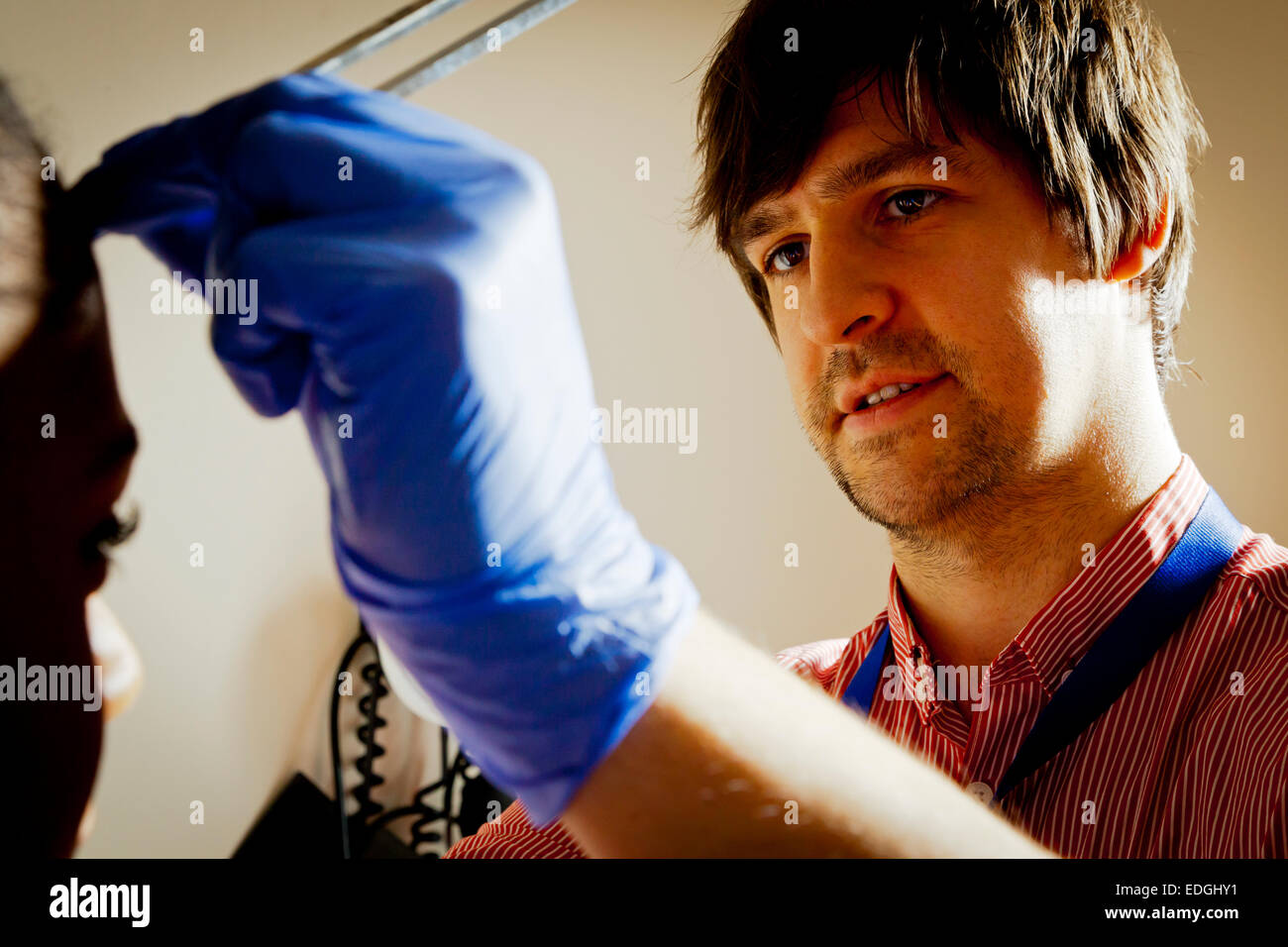 Männlich-NHS-Arzt tragen Schutzhandschuhe, die Untersuchung eines Patienten in einem Krankenzimmer Behandlung Stockfoto