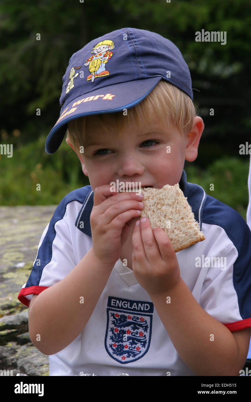 Junge UK im Alter von 4 Essen ein Stück Brot in einem England Footbal Hemd und blaue Kappe. Stockfoto