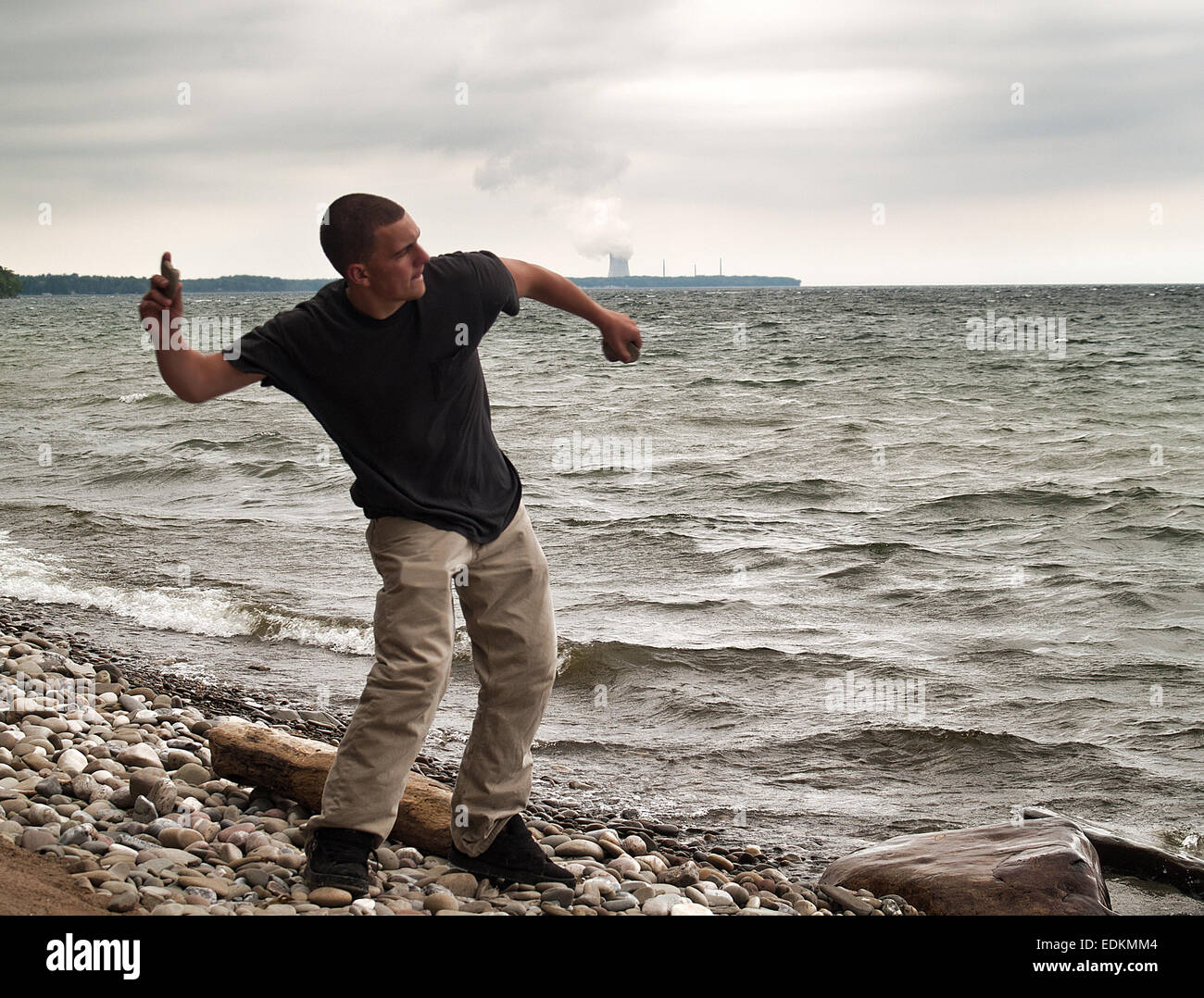 junger Mann skipping Stones auf See Ontario, New York. Neun Meile Punkt erzeugen Kernkraftwerk ist in der Ferne Stockfoto