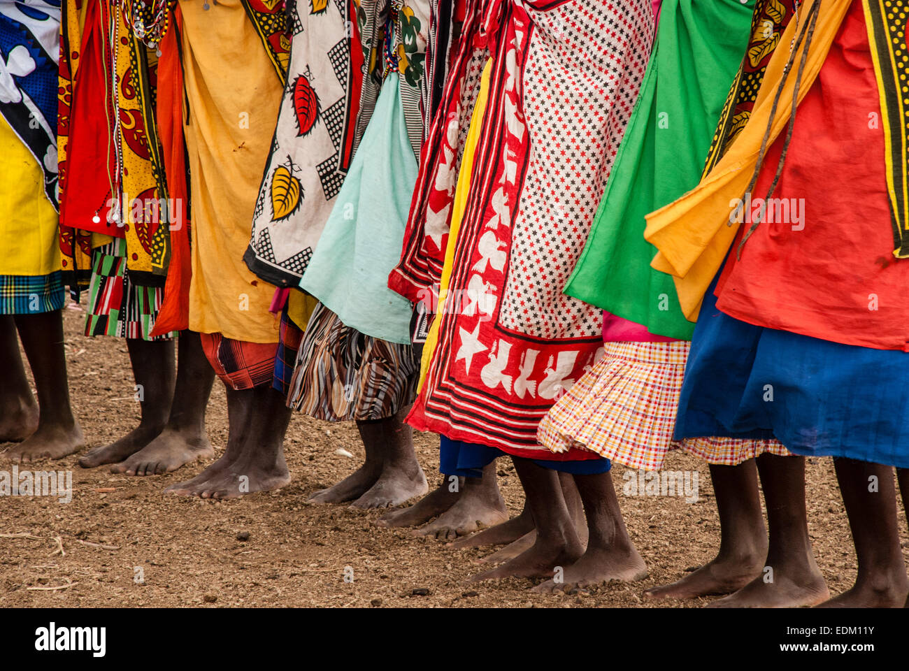 Eine Reihe von barfuß Massai-Frauen tragen die traditionelle Schals genannt Kangas, in einem Dorf in der Nähe der Masai Mara, Ostafrika Stockfoto