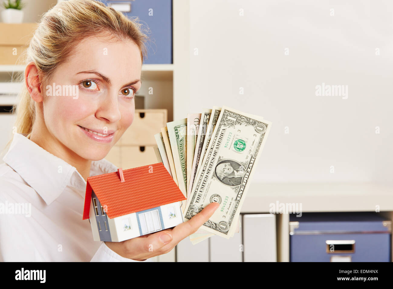 Lächelnde Frau als Immobilienmakler mit kleinem Haus und Dollarnoten Stockfoto