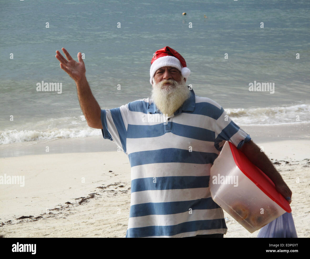 Älterer Mann gekleidet in Nikolausmütze am Strand in der Karibik. Stockfoto