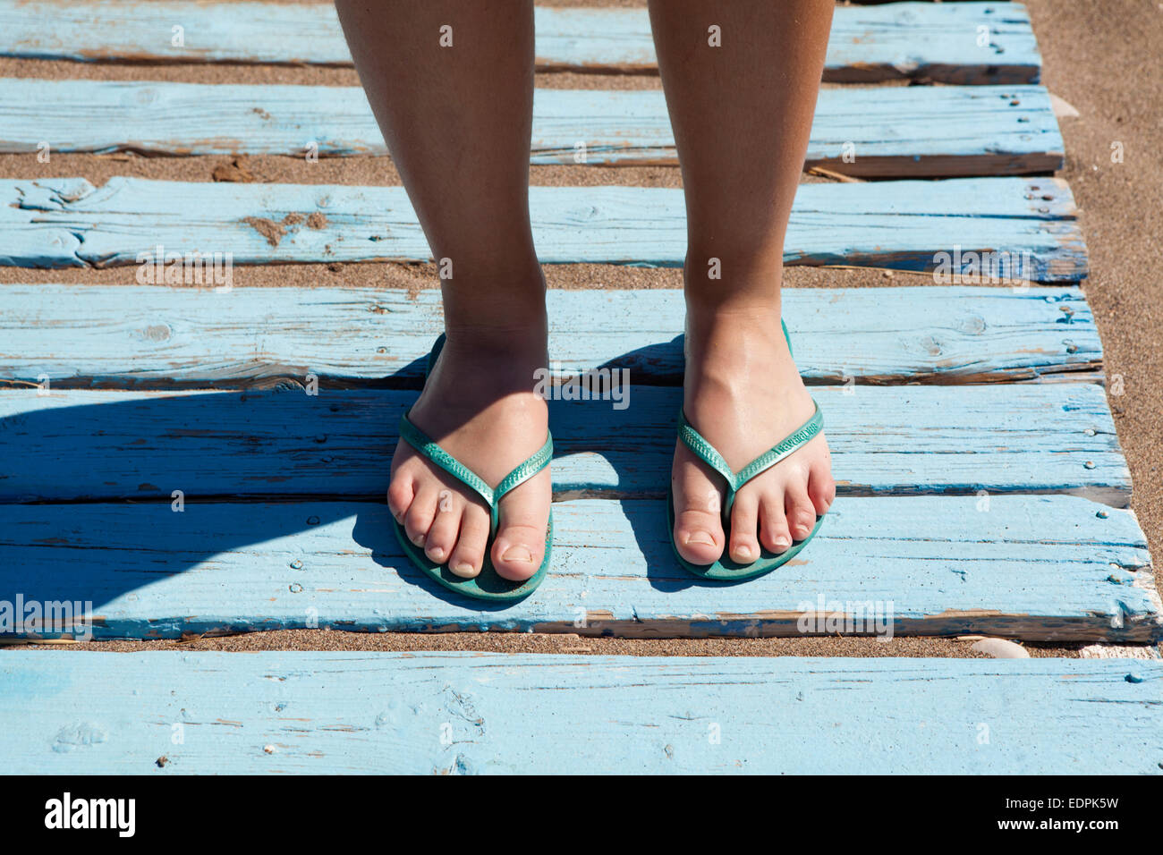 Mädchen Füße tragen Türkis Flip-Flops zu Fuß über hellblauen hölzernen Balken auf dem sand Stockfoto