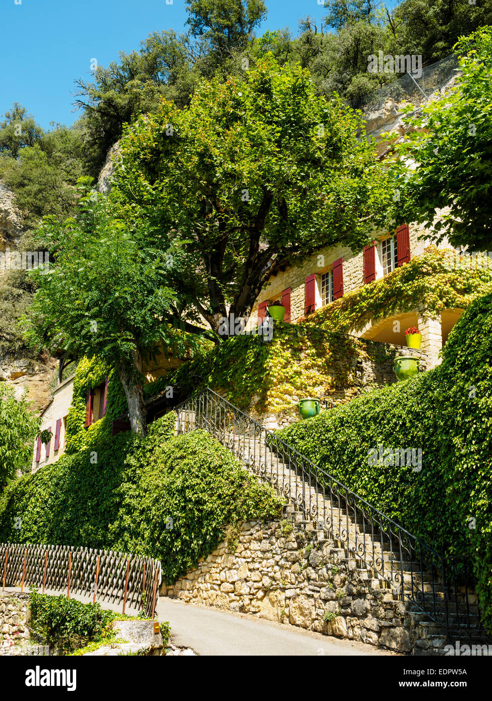 Ein Haus in La Roque-Gageac, direkt neben dem Felsen, umgeben von vielen grünen Pflanzen gebaut. Stockfoto