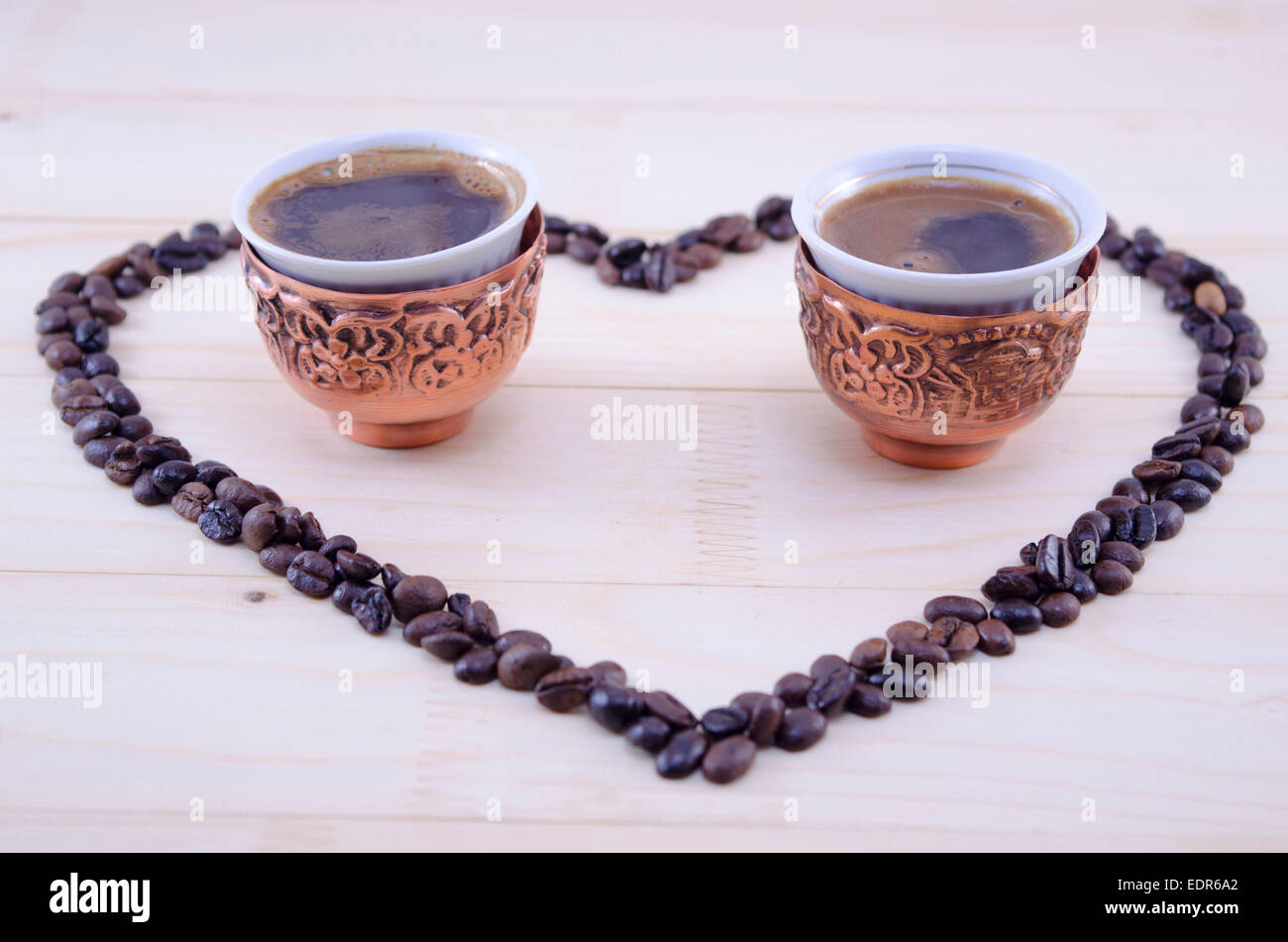 Herz aus rohem Getreide Kaffee mit zwei Tassen in der Mitte platziert auf einem Holztisch Stockfoto