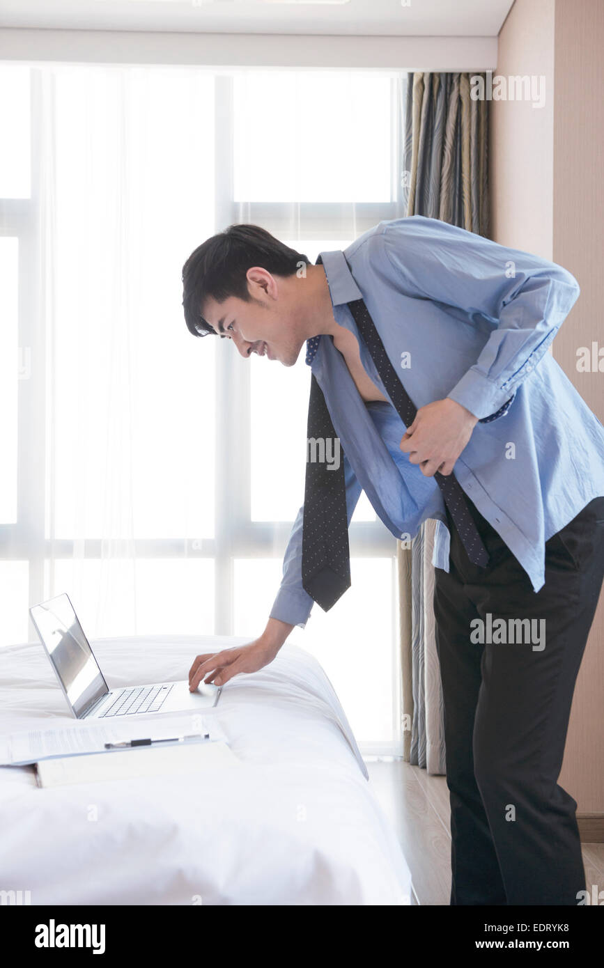 Junger Mann beim anziehen, während mit laptop Stockfoto