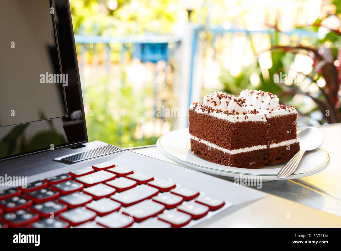 Schokoladekuchen mit weiße Creme auf die Spitze und Notebook-Computer im Haus Stockfoto