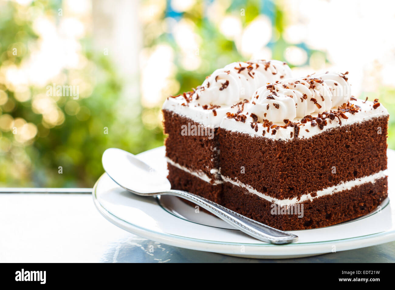 Schokoladekuchen mit weiße Creme obendrauf und Löffel auf Teller und Bokeh im Hintergrund Stockfoto