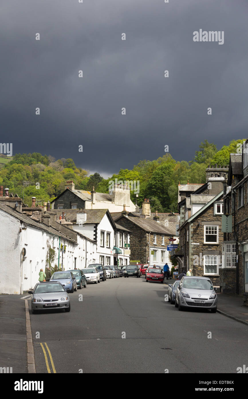 Church Street in Ambleside, Cumbira, durch einen kurzen Sonnenstrahl beleuchtet, während dunkle Wolken Seenplatte Regen drohen. Stockfoto