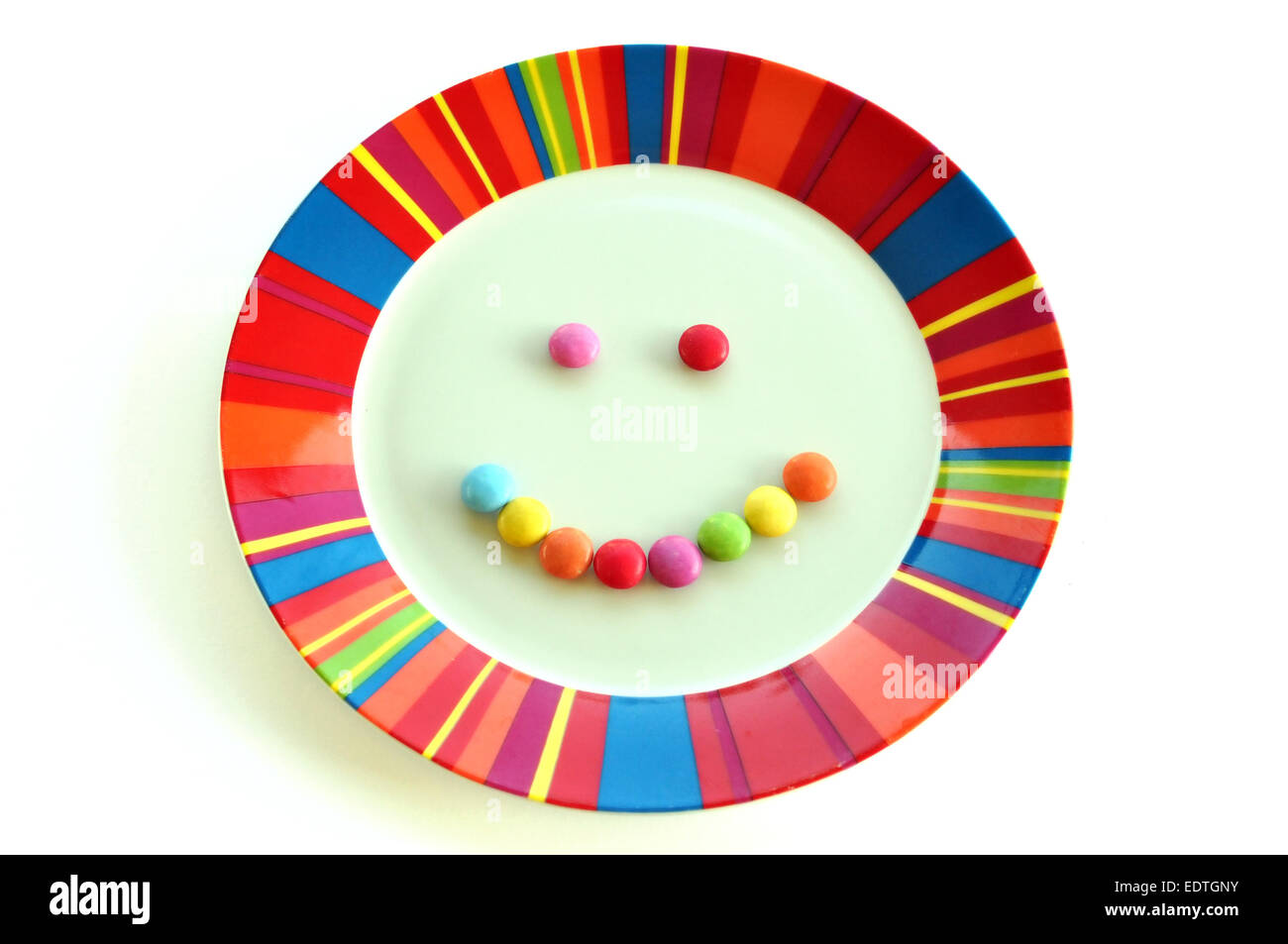 Lächelndes Gesicht aus Süßigkeiten und bunte Platte auf weißem Hintergrund gemacht. Kinder Dessert Essen glücklich essen. Stockfoto
