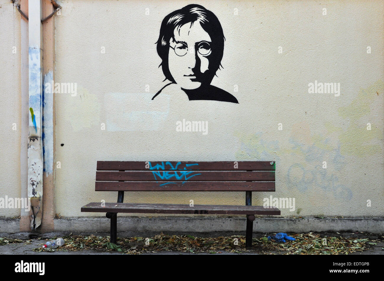 Berühmte Musiker John Lennon von den Beatles Porträt Schablone Graffiti auf strukturierte Wand und Holzbank. Stockfoto
