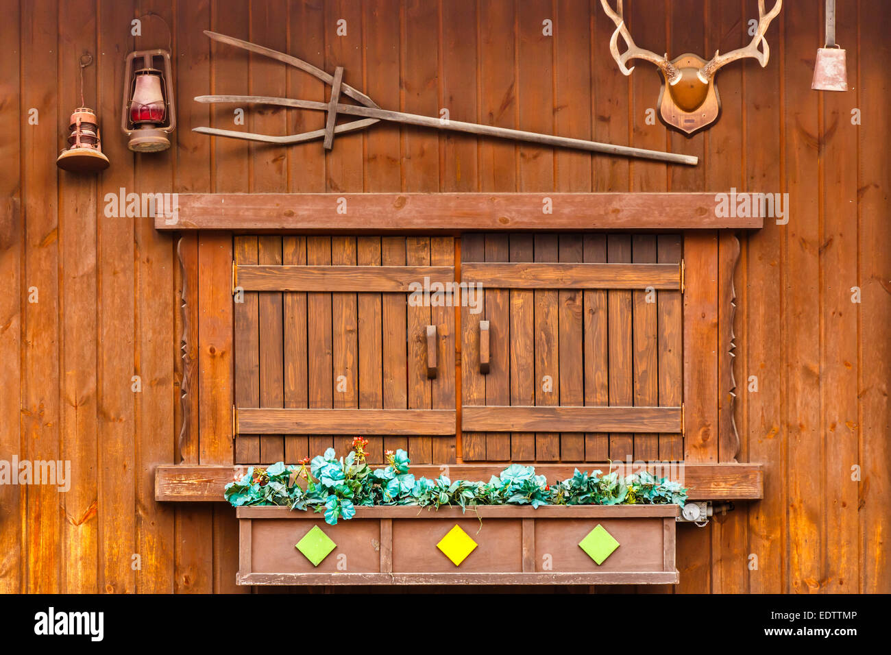 Holz-Fenster auf Holzhaus und dekoriert mit Pflanzen, Geweih, Lampe, Glocke und Dreizack Stockfoto