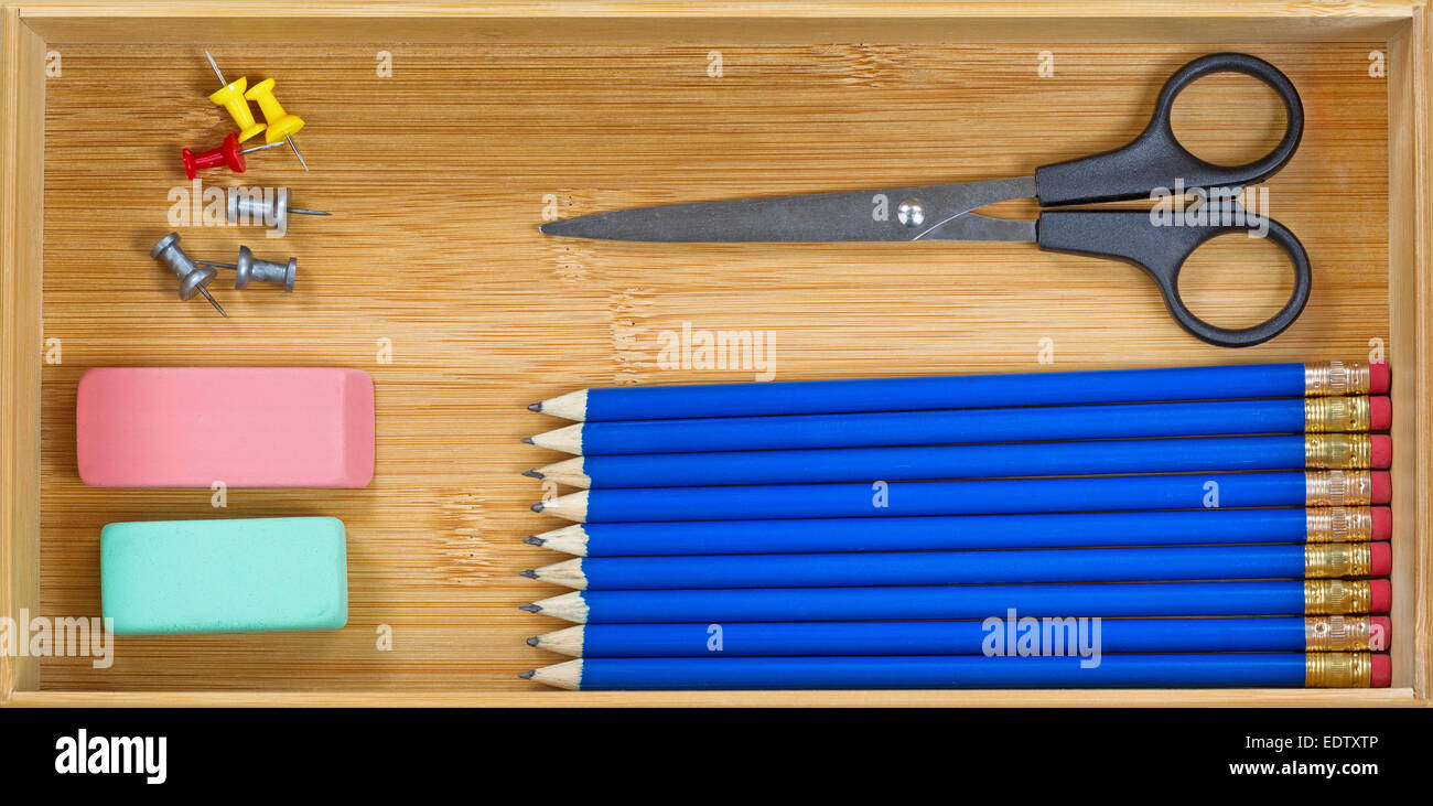 Draufsicht der blauen Farbstifte, aufgereiht, Radiergummi, Schere und Stift Reisszwecken in hölzernen Schreibtisch-Schublade Stockfoto