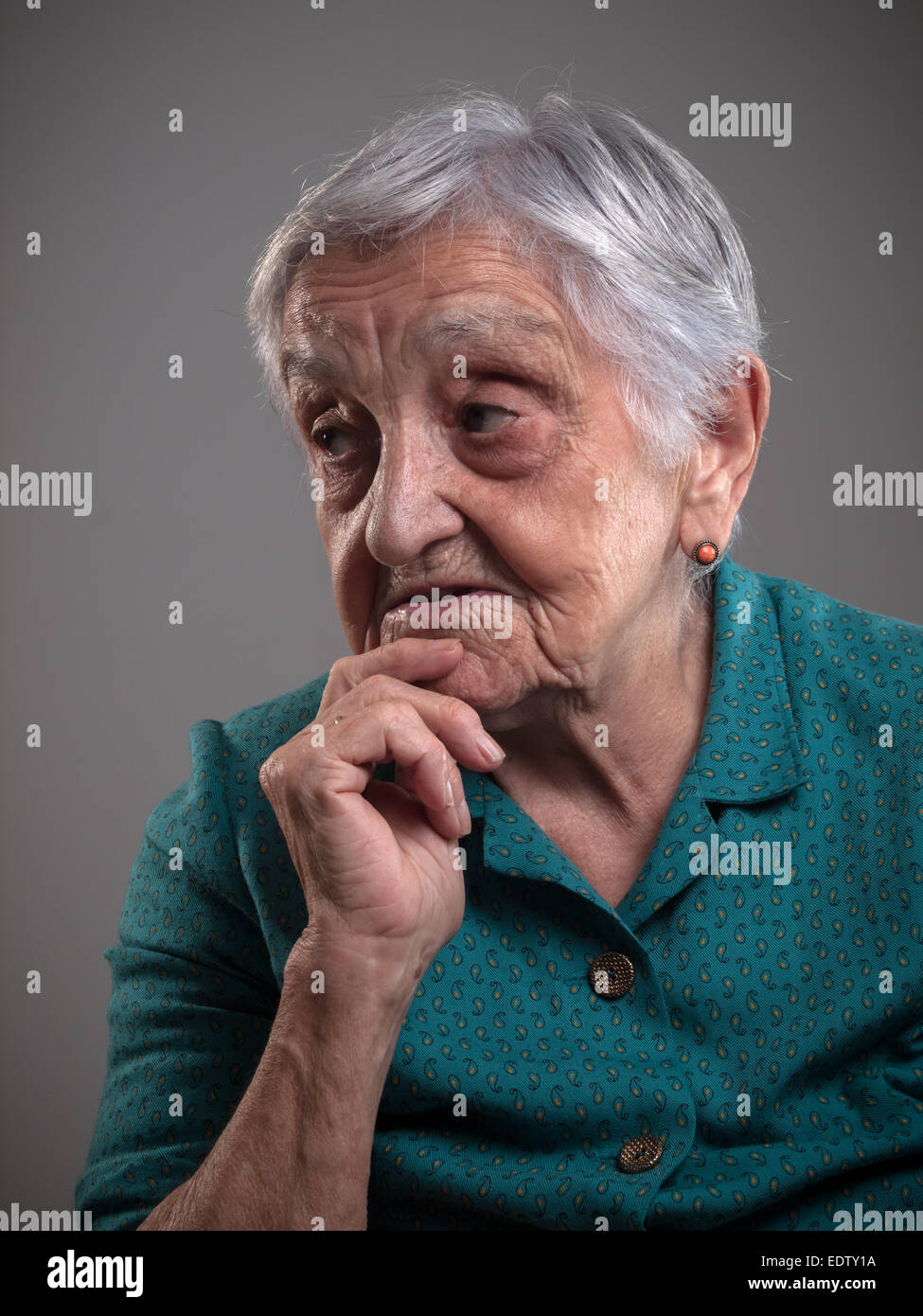 Ältere Frau Porträt in einem Studio gedreht. Alte Frau hatte ihre Hand am Kinn und sucht beiseite. Stockfoto