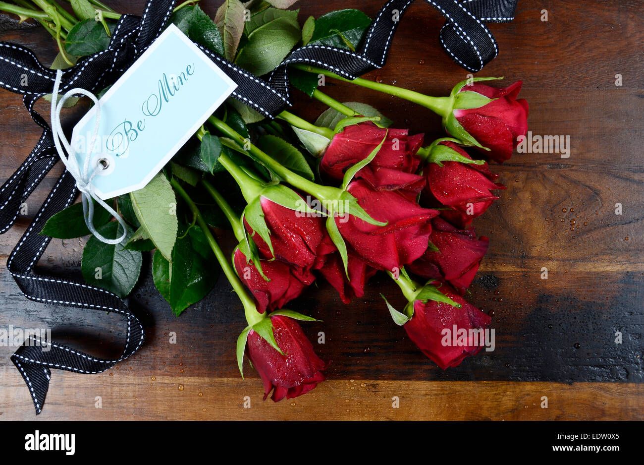 Happy Valentinstag rote Rosen auf dunkle recycelt Holz Hintergrund - overhead mit Be Mine blass blauen Geschenkanhänger. Stockfoto