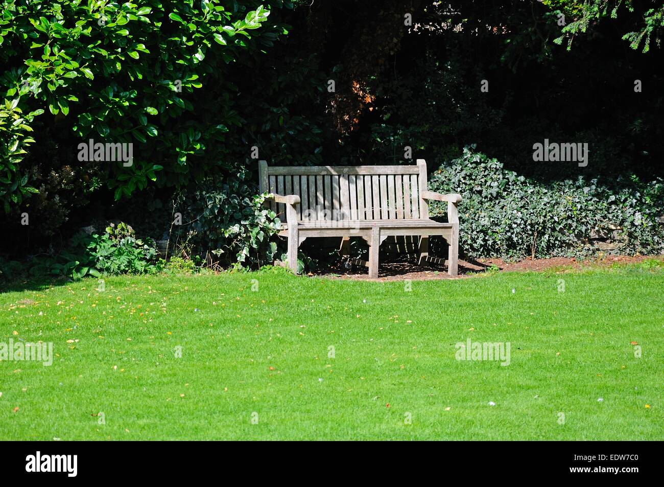 Holzbank am Rande des Rasens auf dem Gelände der Abtei, Tewkesbury, Gloucestershire, England, Vereinigtes Königreich, West-Europa. Stockfoto