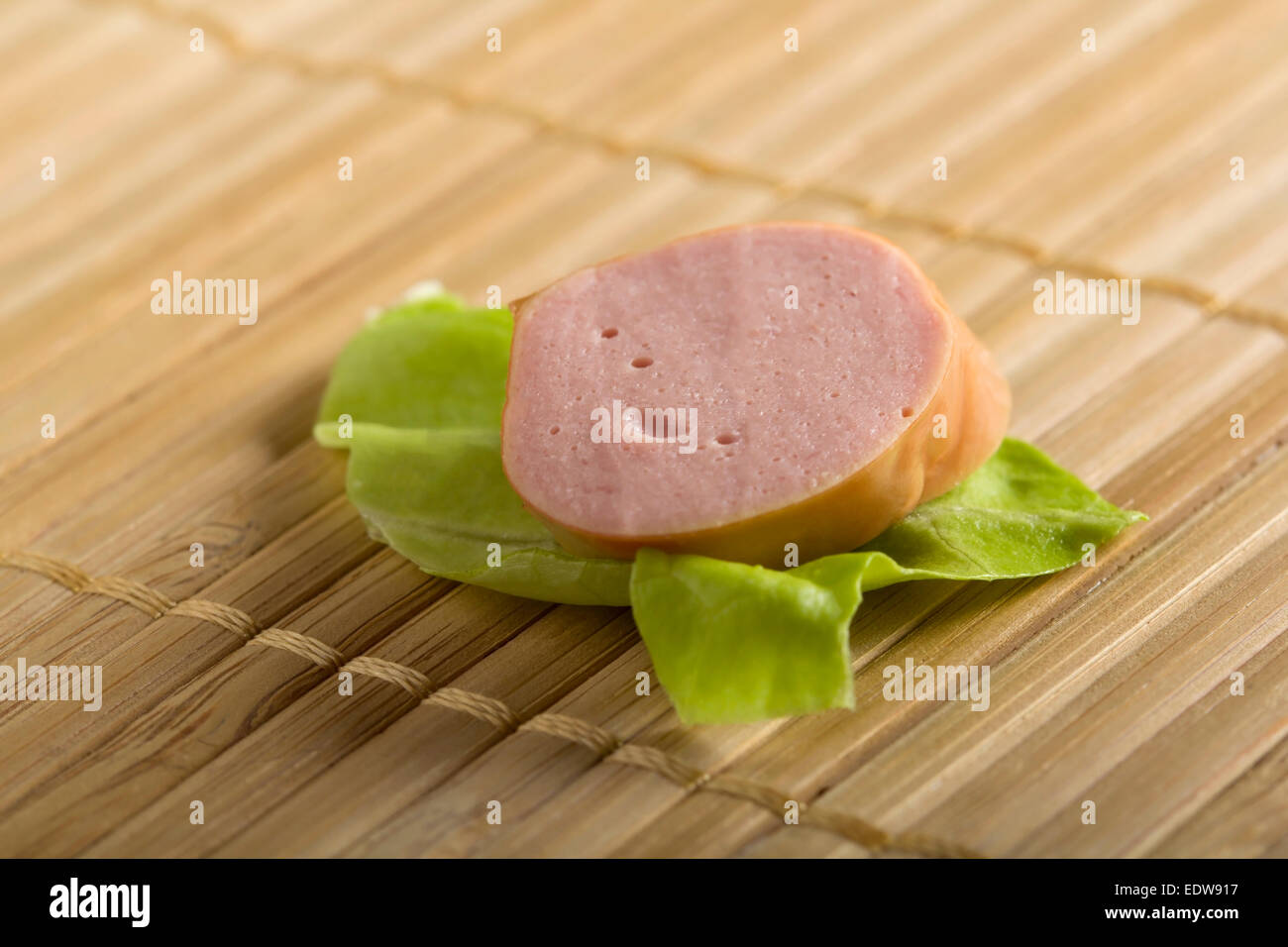 Eine Wurst Scheibe auf Salatblatt über Bambus Hintergrund Stockfoto