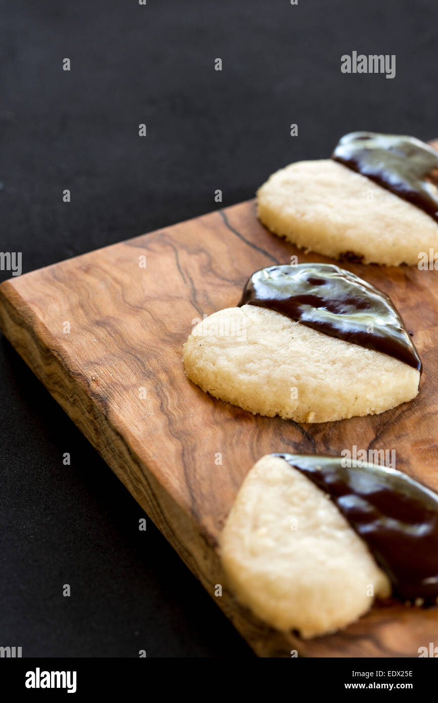 hausgemachte Schokolade getaucht Herz Kekse oder Cookies auf Oliven Holzplatte auf schwarzem Hintergrund Stockfoto