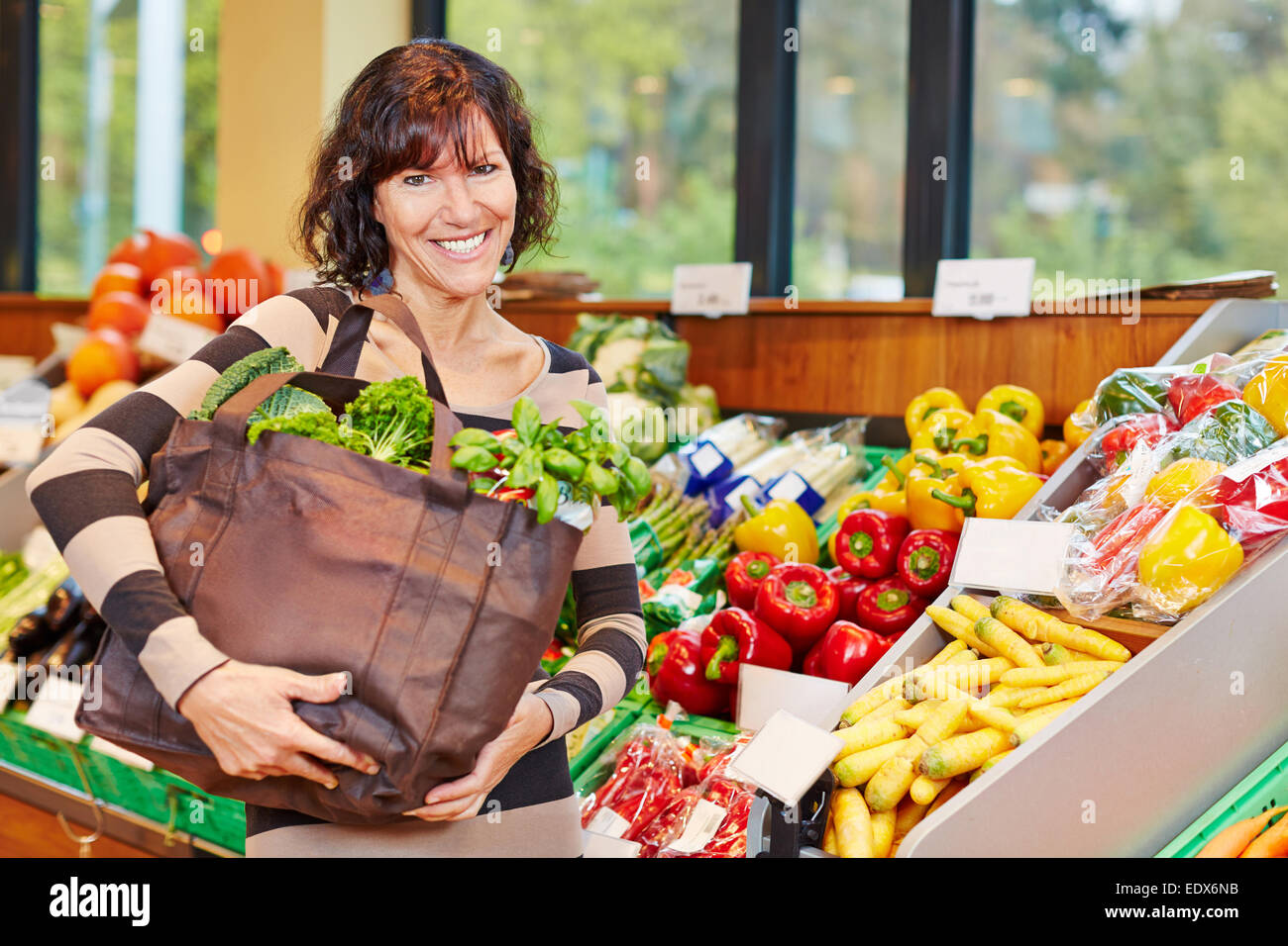 Lächelnde ältere Frau mit Tasche voll mit frischem Gemüse in einem Supermarkt Stockfoto