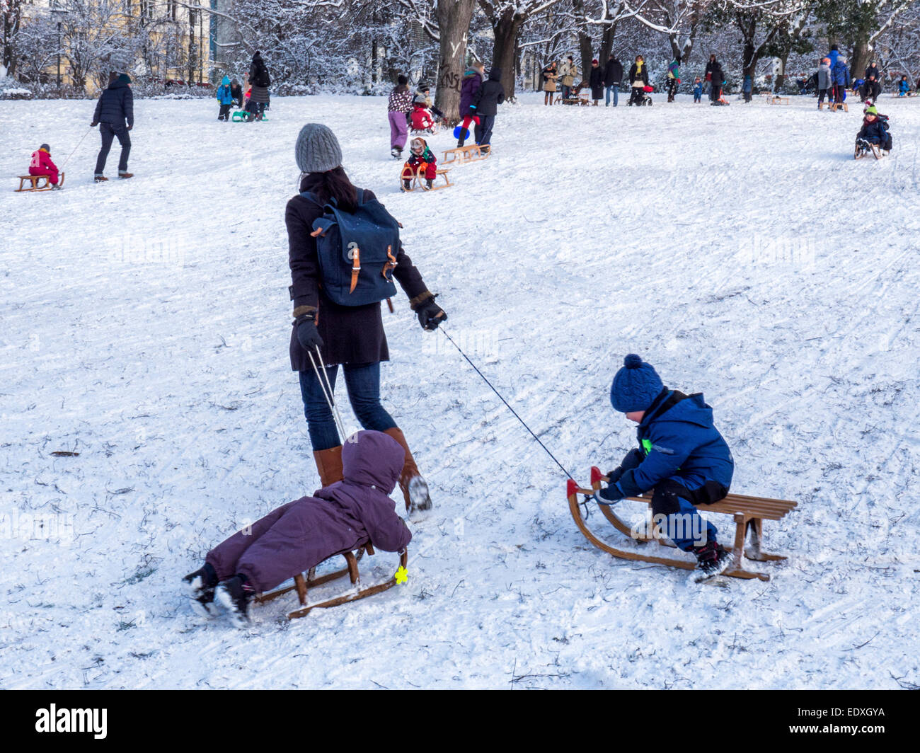 Frau junge Kinder mit zwei Schlitten ziehen, nach schweren Winterschnee im öffentlichen Park, Berlin Stockfoto