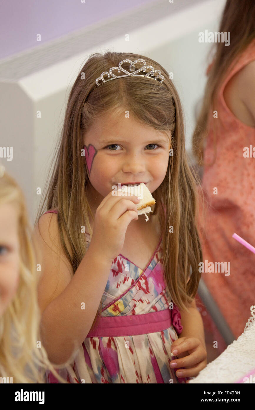 hübsches Geburtstagskind verkleidet mit Tiara ein Sandwich zu essen Stockfoto