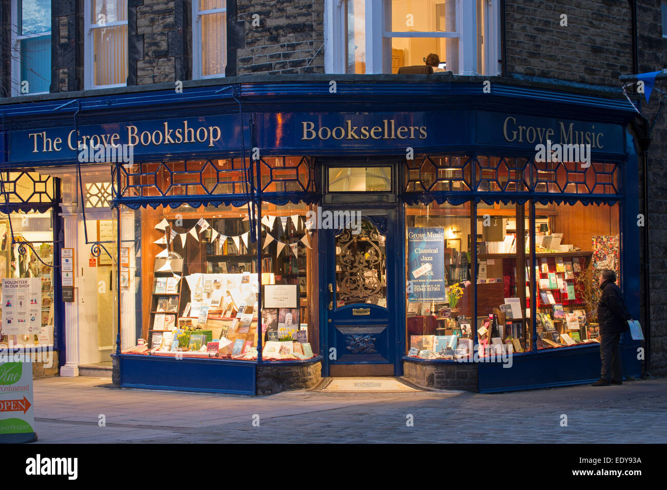 Mann draußen schaut sich die Schaufenster Bücher in der Grove Buchhandlung (traditionelle Buchhandlung, einladendes goldenes Leuchten) - Ilkley, West Yorkshire, Großbritannien. Stockfoto