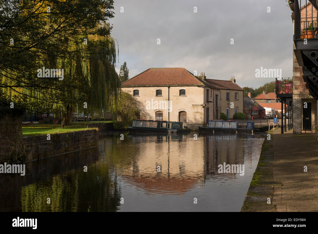 Renovierte, historische Lagergebäude und 2 angelegte Boote, die in den ruhigen Wasser des Canal Basin wider - Ripon Kanal, North Yorkshire, England, UK. Stockfoto