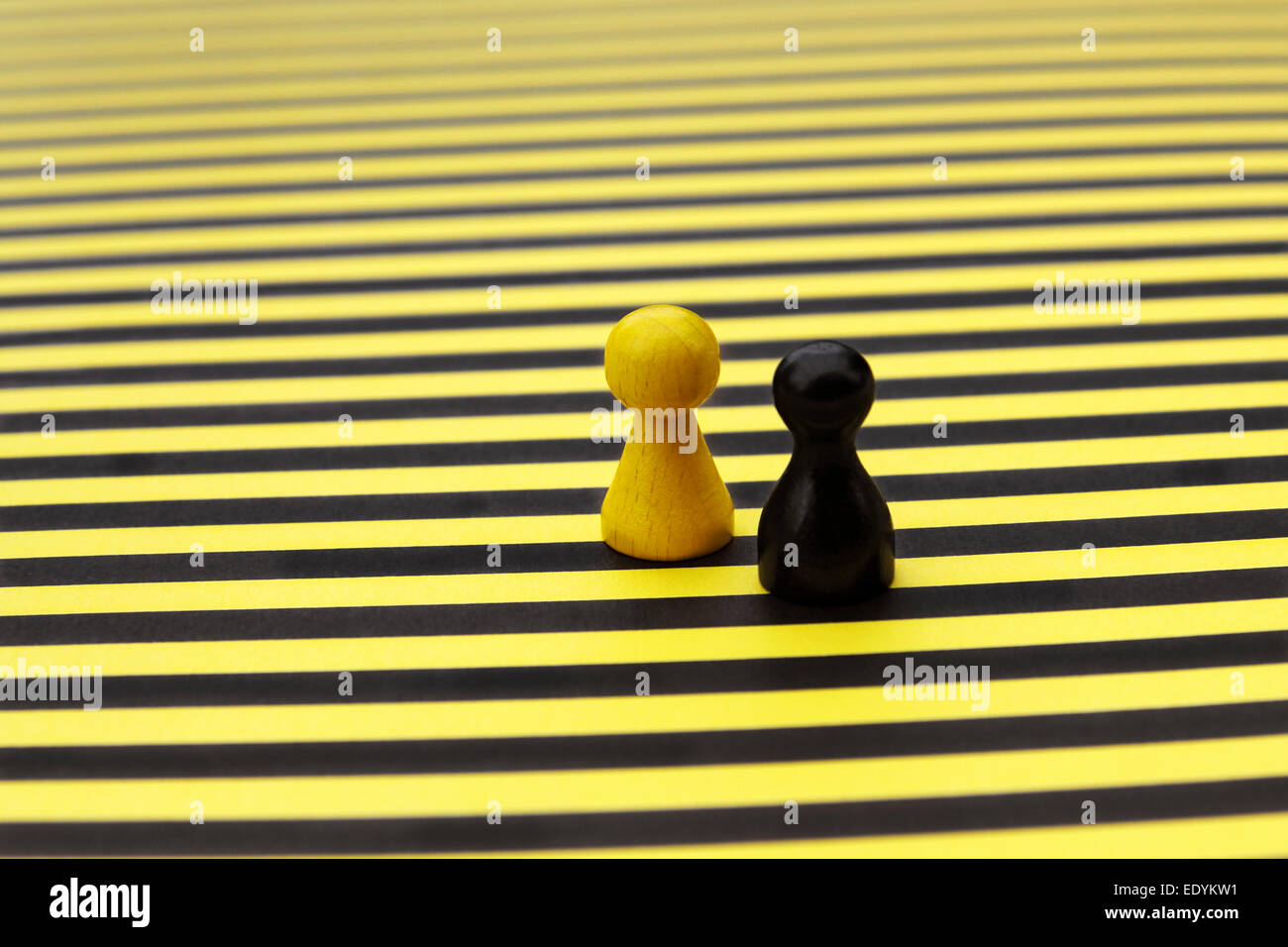 Eine gelbe und eine schwarze Spielsteins, nebeneinander, auf einem gelb-schwarz gestreiften Brett Stockfoto
