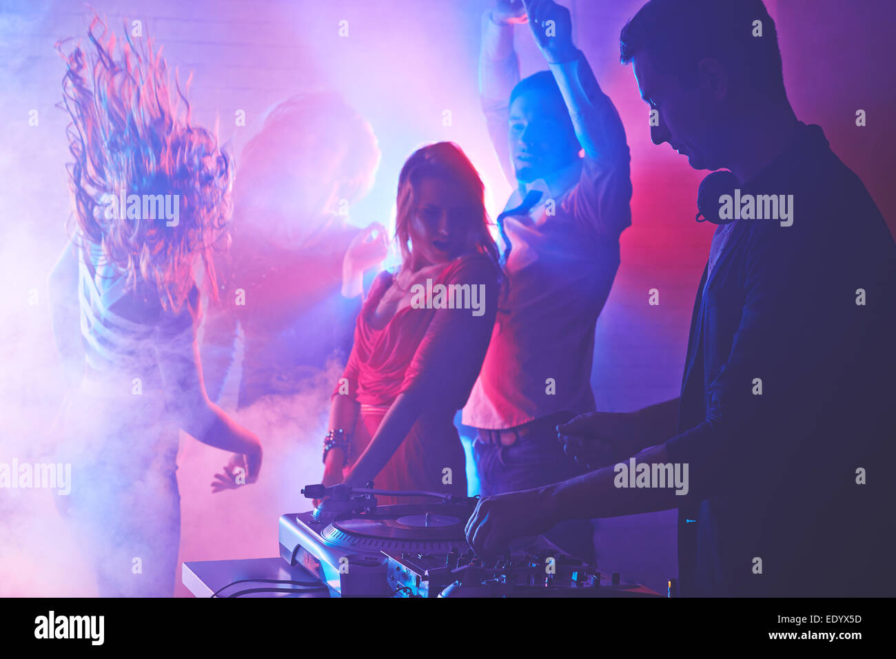 Männliche DJ mischen Sounds mit energetischen Mädchen und Kerl tanzen auf Hintergrund Stockfoto