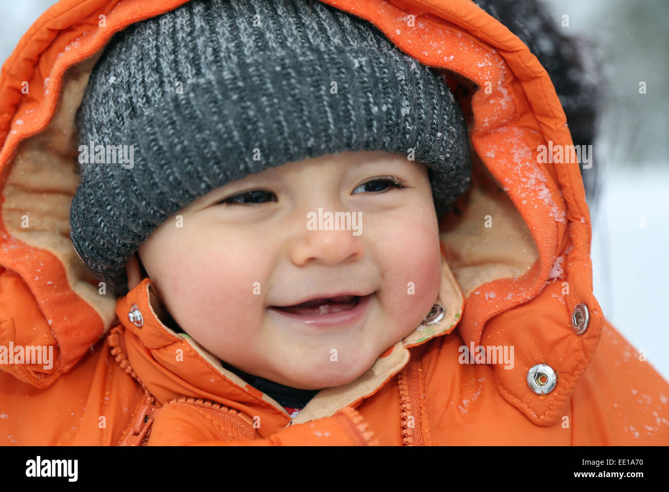 Porträt eines lächelnden Babys mit Schnee im Winter mit Mütze und Winterkleidung Stockfoto