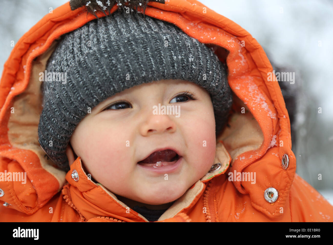 Portrait eines lächelnden Babyjungen mit Schnee im Winter mit Mütze und Winterkleidung Stockfoto