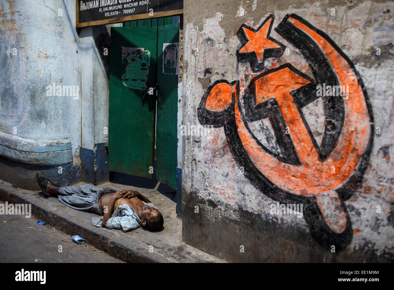 Eine Person schläft unter einer kommunistischen Partei Symbol in dunklen Gasse von Kolkata, Indien Stockfoto