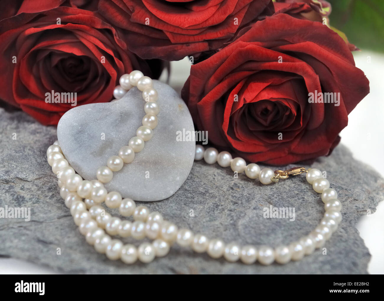 Kette aus Perlen auf steinerne Herz mit roten Rosen Stockfoto