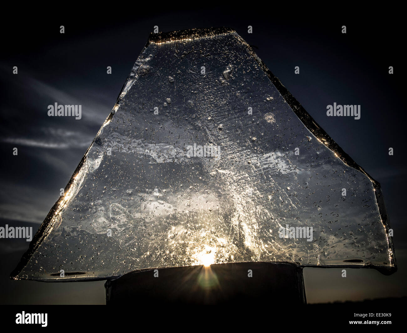 Ein Splitter des gefrorenen Pfütze Eis auf einem Zaunpfahl mit tief stehender Sonne dahinter stehen. Bunten Bild. Stockfoto