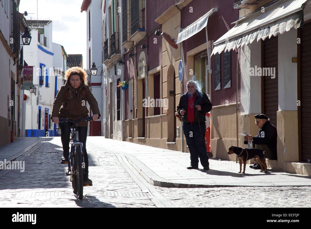 Leben auf der Straße, Córdoba, Andalusien, Spanien: Frau Radfahren, Mann Rauchen, Mann in Barett mit Hund Zeitung lesen Stockfoto