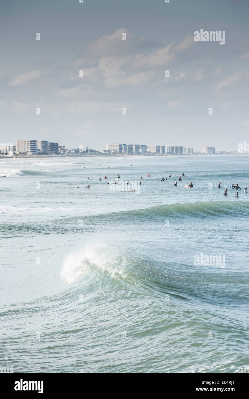 Viele Surfer in einer Linie bis zu einem Wave als dünung Walzen verfangen, indem mit dem Daytona Beach, Florida Skyline im Hintergrund wartet. Stockfoto