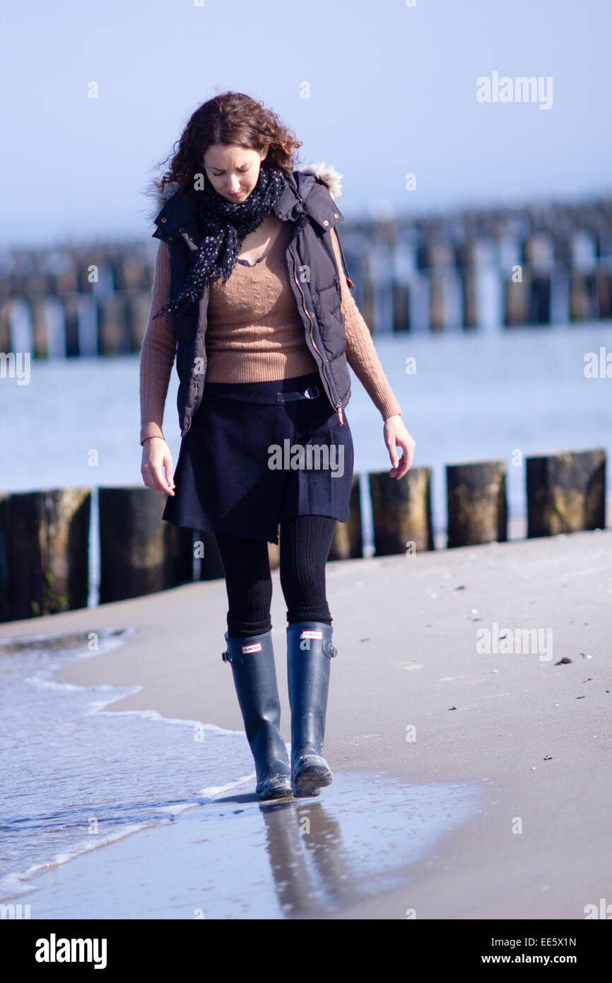 Frau zu Fuß an einem Strand in der Nähe von Rostock, Norddeutschland mit hölzernen See Verteidigung hinter ihr. Stockfoto