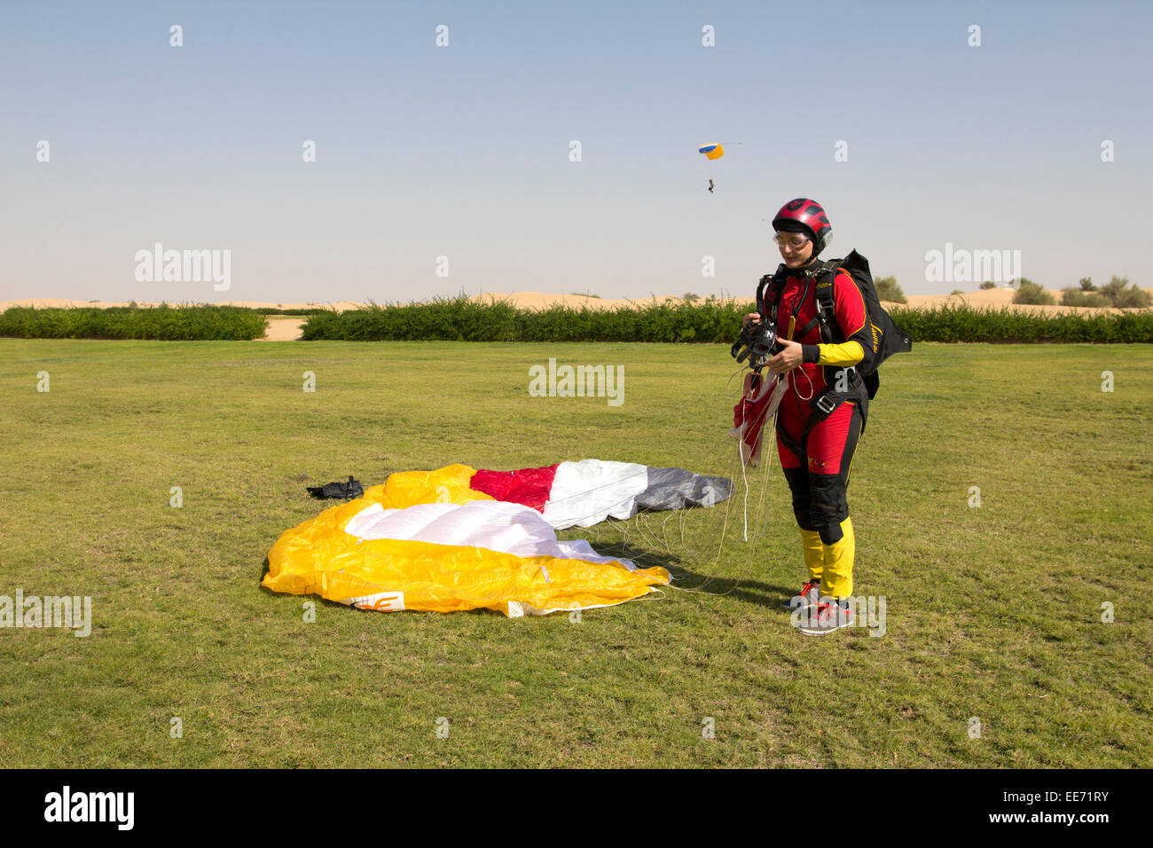 Diese Fallschirmspringen Mädchen gerade gelandet zu retten mit ihrem Baldachin auf der Rasenfläche. Die Fallschirmspringer hinter ihr nähert sich die Sanddünen. Stockfoto