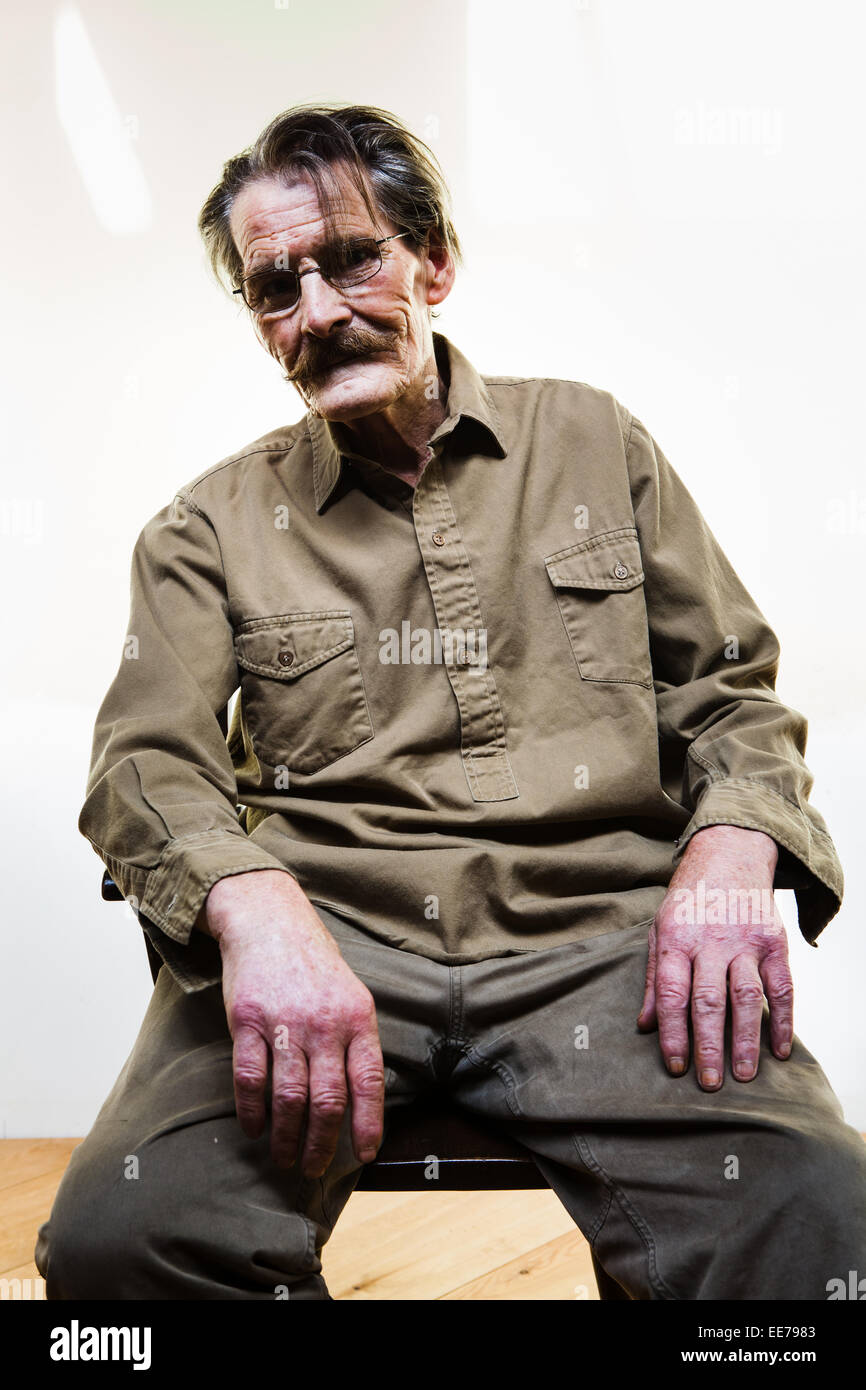 Der Mensch in seiner 60er Jahre mit Schnurrbart in einem Sessel sitzend. Khakifarbene Hemd und Hose. Stockfoto