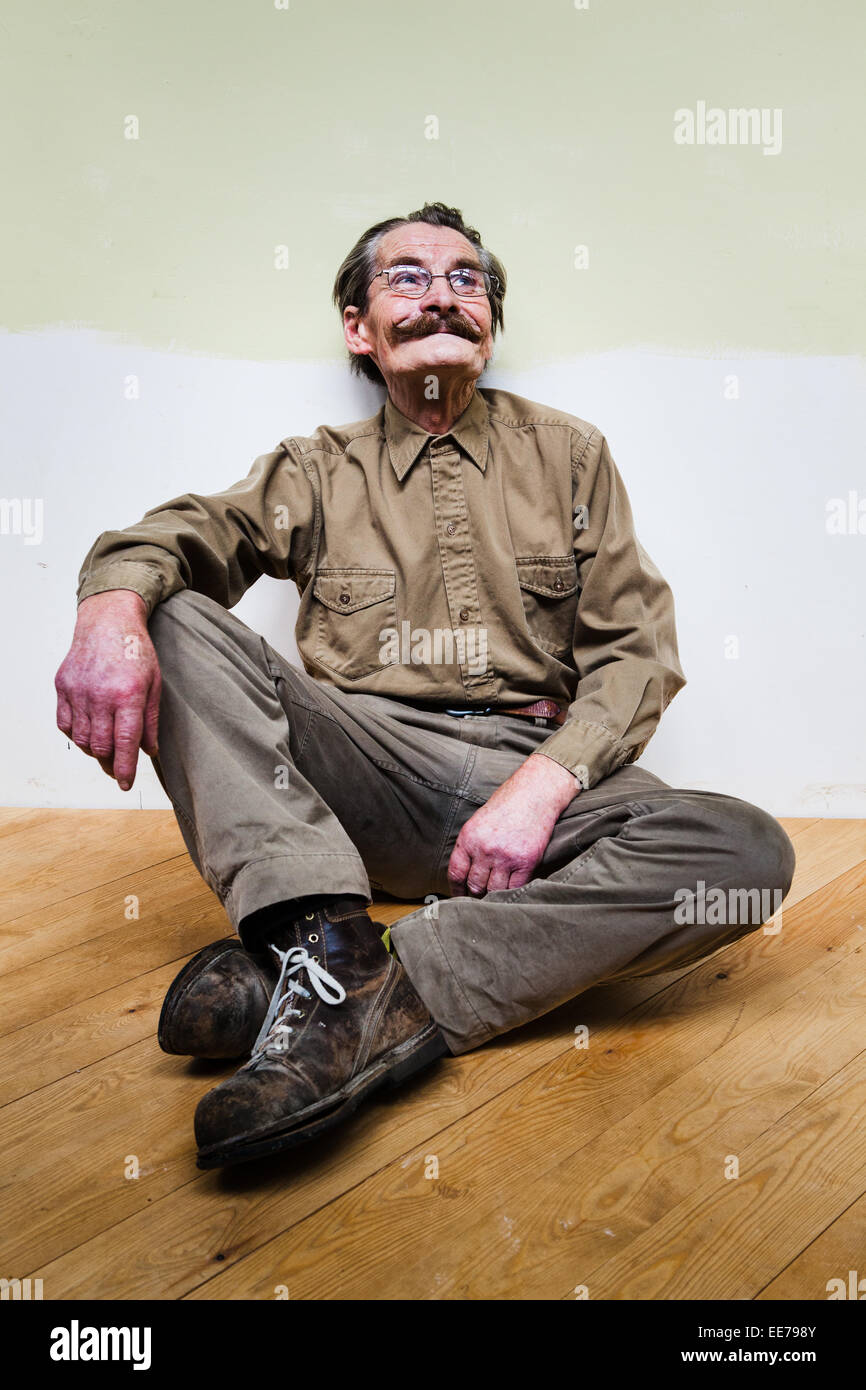 Der Mensch in seiner 60er Jahre mit Schnurrbart tragen khakifarbene Hemd und Hose auf dem Boden sitzen. Stockfoto