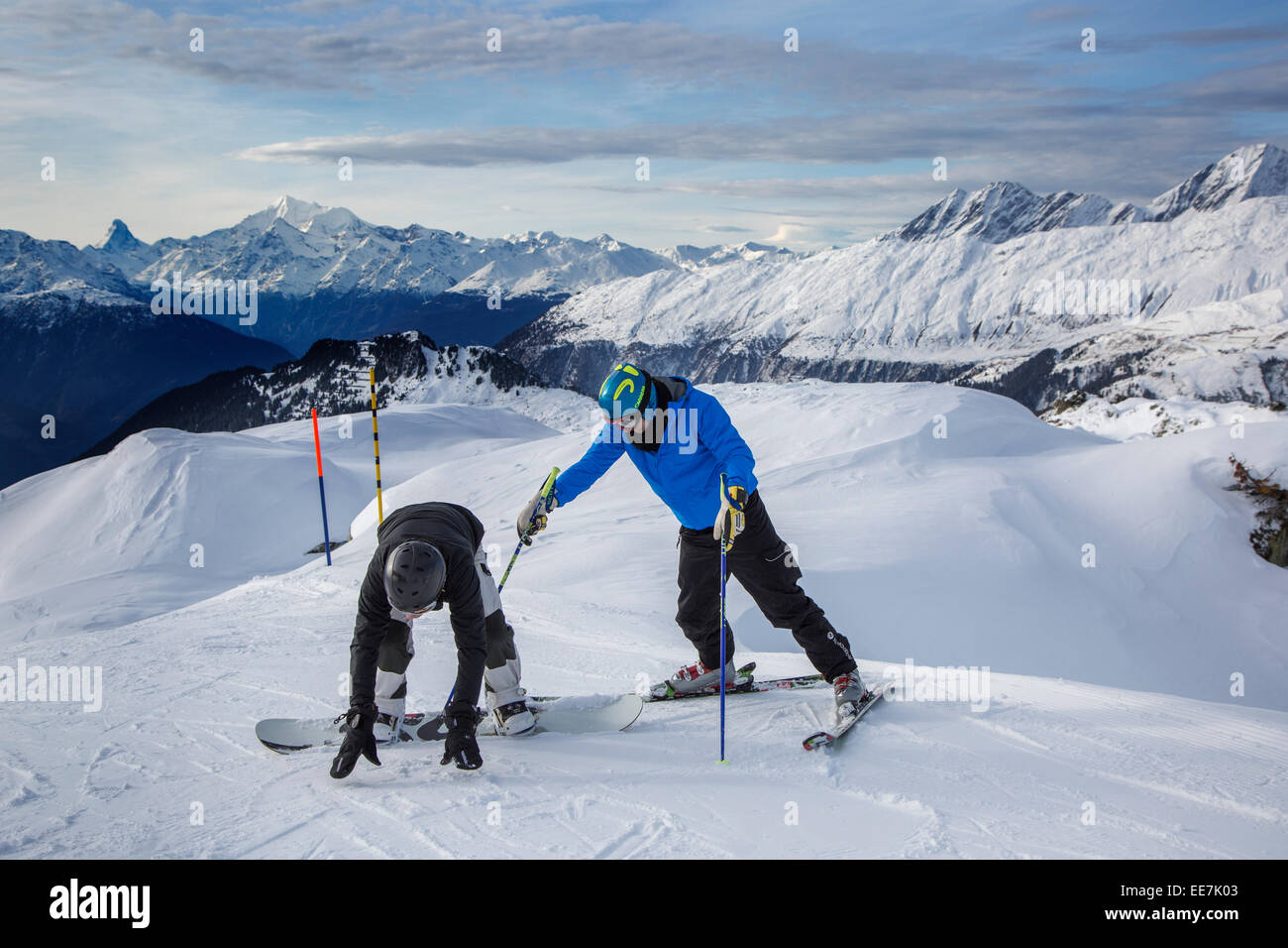 Skifahrer, die helfen, ungeschickt Snowboarder mit Skihelm auf Skipiste im Wintersportort in den Alpen aufrecht stehen Stockfoto