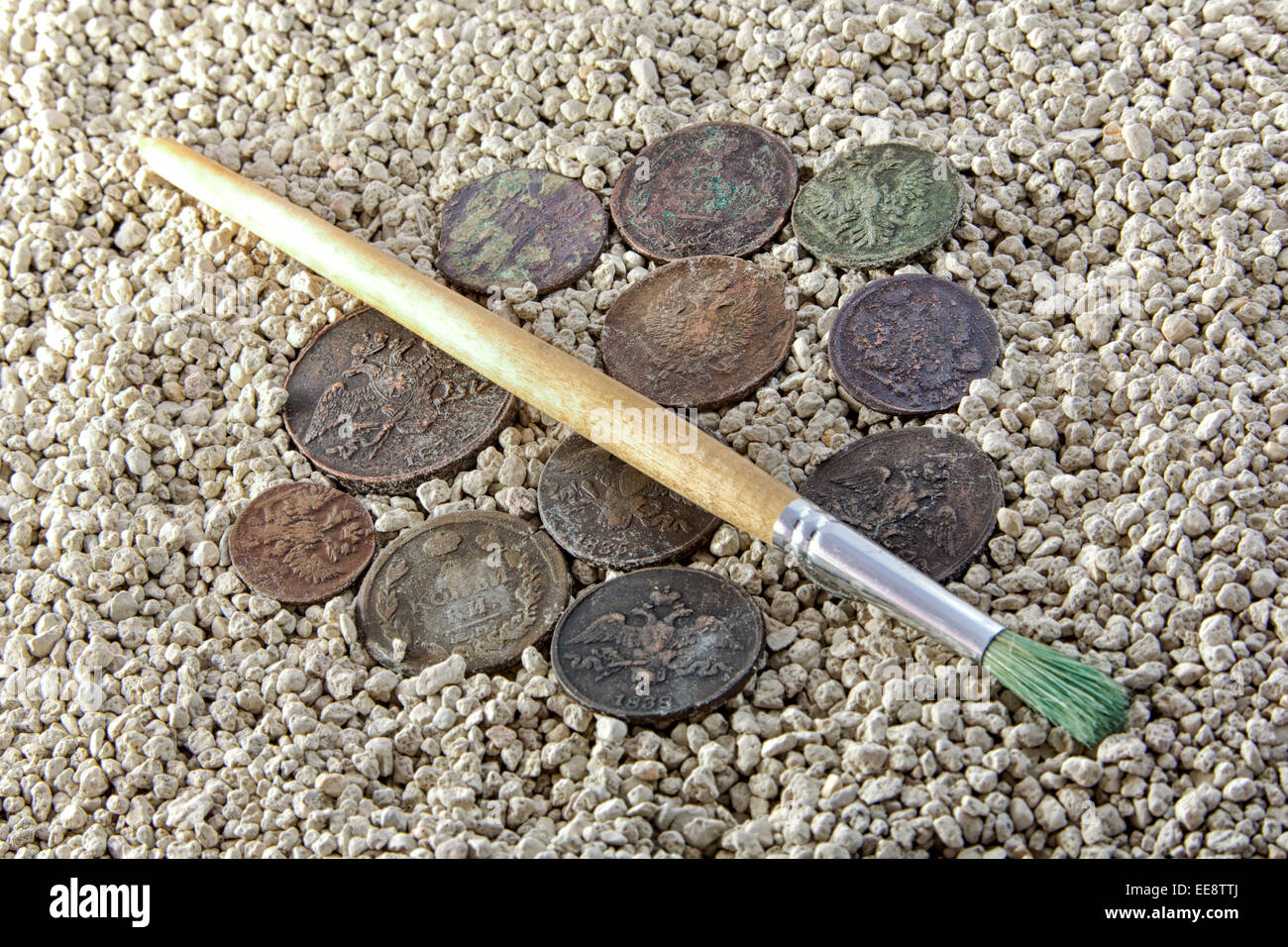 alte Münzen in den Sand und Pinsel löschen Stockfoto