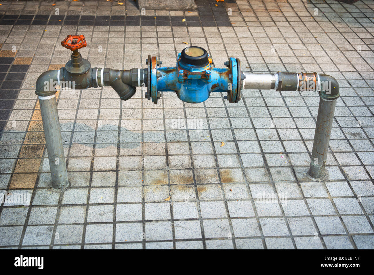 Wasserrohre mit einem Messgerät und Haupt-Absperrventil, ragen aus dem Gehsteig entlang einer öffentlichen Straße. Stockfoto