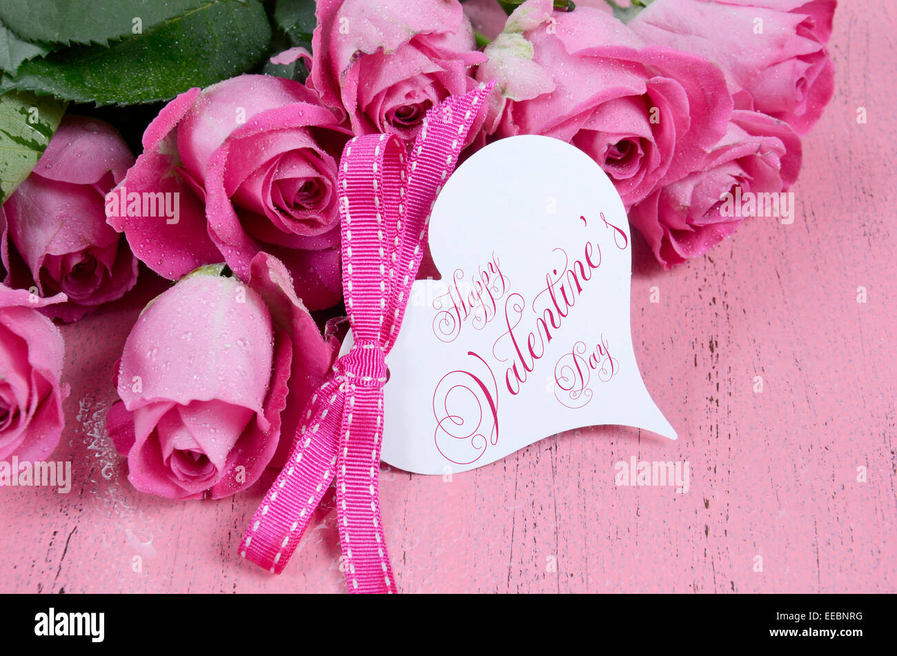 Rosa Rosen auf rosa Holz Hintergrund Closeup mit Happy Valentines Day Herz Form Geschenkanhänger. Stockfoto