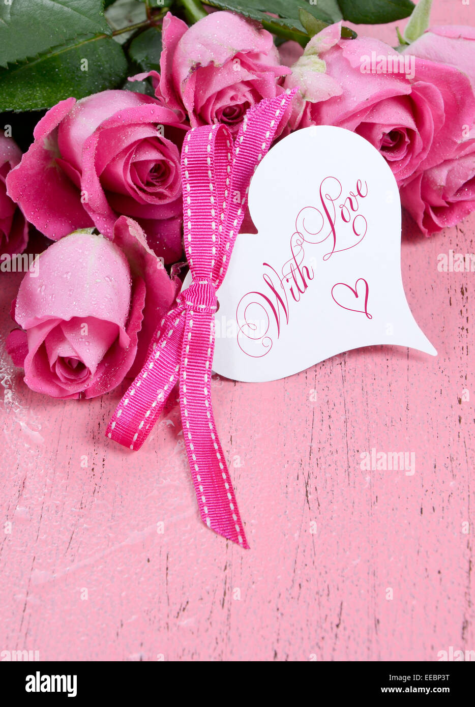 Rosa Rosen auf rosa Holz Hintergrund Closeup mit Happy Valentines Day Herz Form Geschenkanhänger, vertikal mit Textfreiraum. Stockfoto
