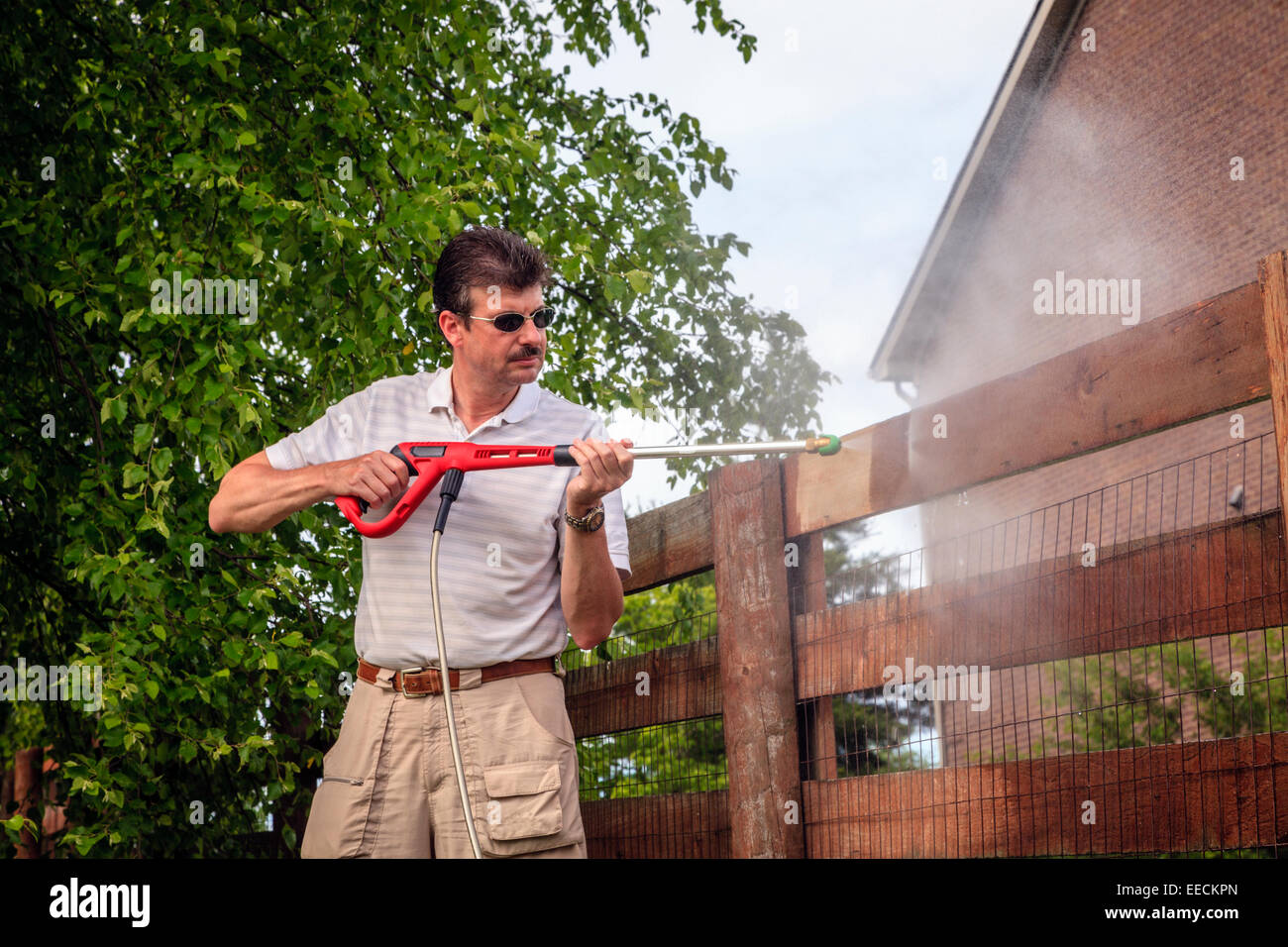 Ein Mann ist Holzzaun mit elektrischer Hochdruckreiniger reinigen. Stockfoto