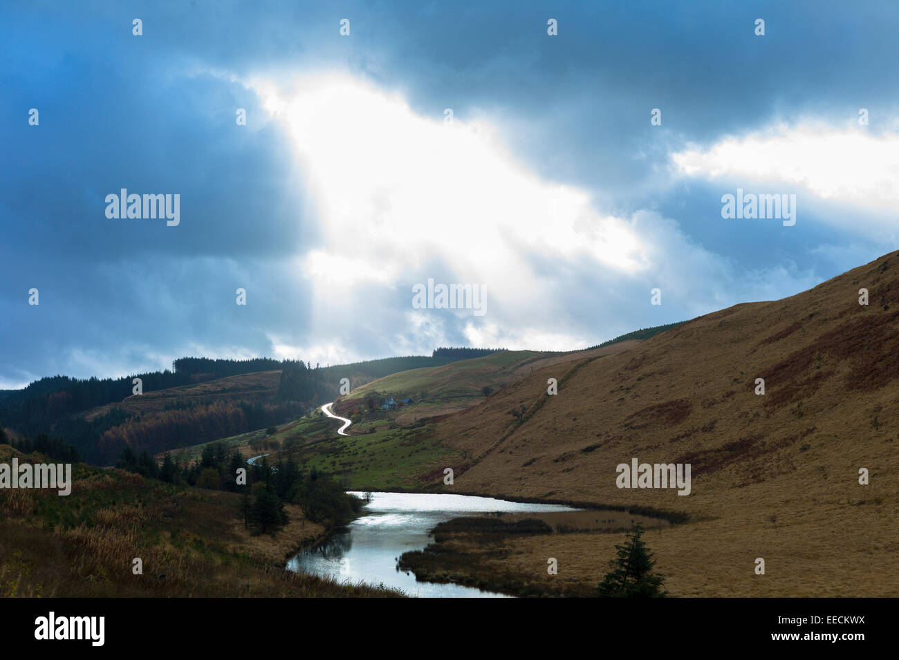 Sonnenlicht durch Wolke scheint auf Fluss und leere Straße entlang eines Tales in den Brecon Beacons-Gebirge in Wales, UK Stockfoto