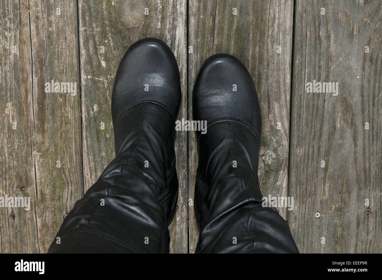 Woman's Füßen trug hohe schwarze Stiefel auf ein unbehandeltes Holz. Stockfoto