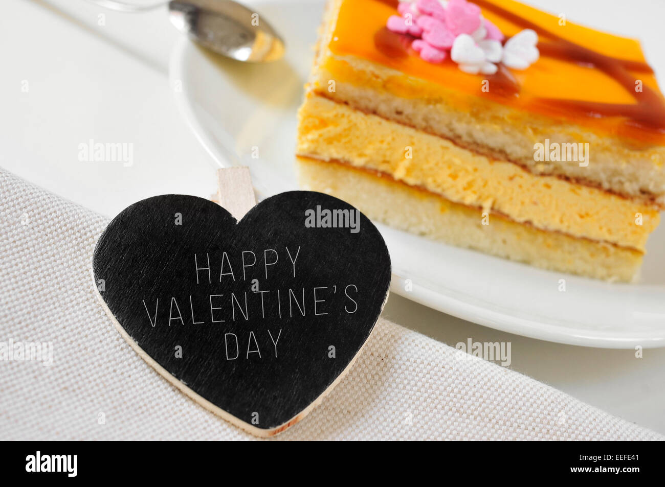der Satz glücklich Valentinstag, geschrieben in einer Herzform Tafel und ein Stück Kuchen auf einem gedeckten Tisch Stockfoto