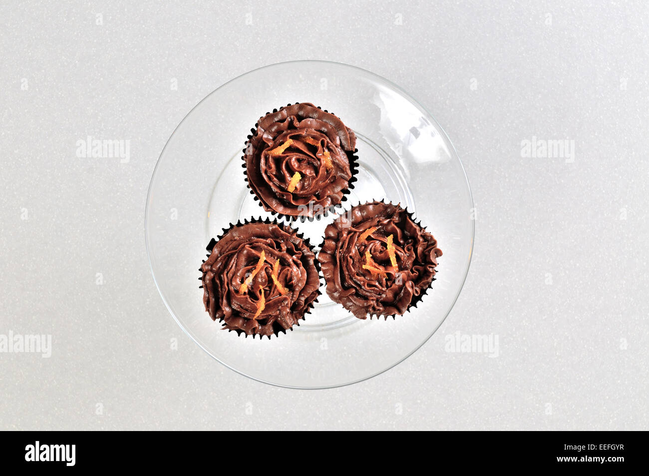 Drei Schokolade Cupcakes mit orange Streusel auf einer Glas-Platte. Stockfoto